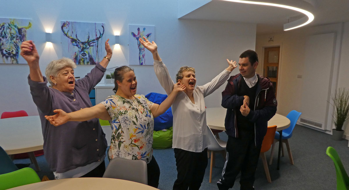 Three individuals stand in a room, raising their arms in celebration or excitement.